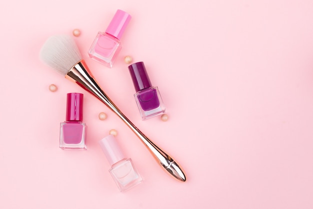 Makeup brush and nail polishes on a pink background. Close-up with space for text.