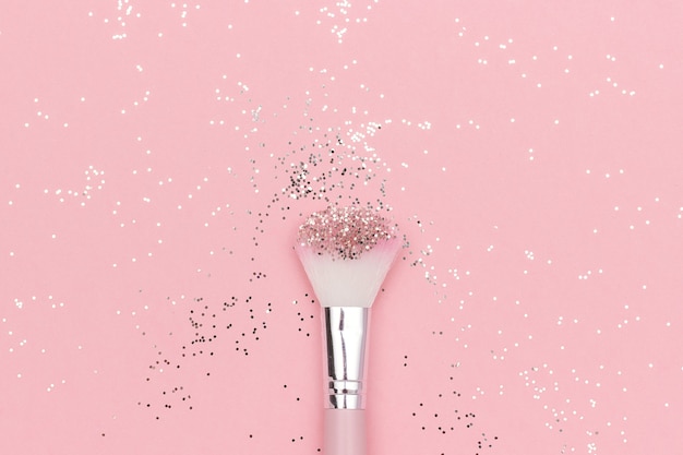 Makeup brush and shiny sparkles on pastel pink. Festive magic makeup concept.