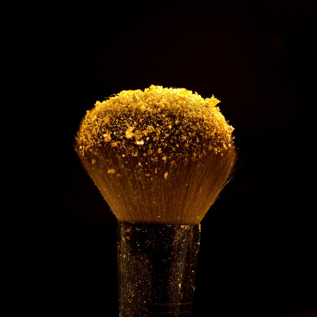 Spazzola di trucco con polvere cosmetica dorata che si spande su fondo nero