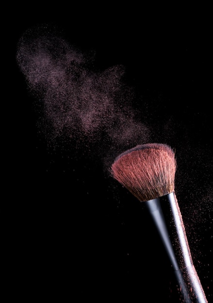 Makeup brush with pink powder dust on black background