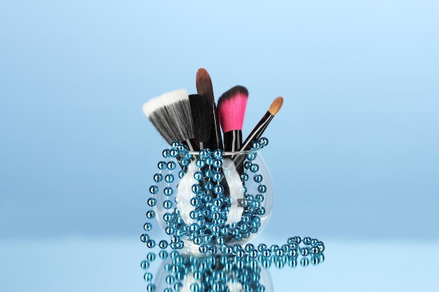 Photo makeup brushes in a bowl with pearl necklace on blue background