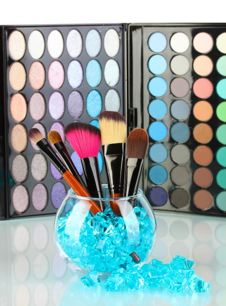 Makeup brushes in a bowl with stones on palette of shadows background