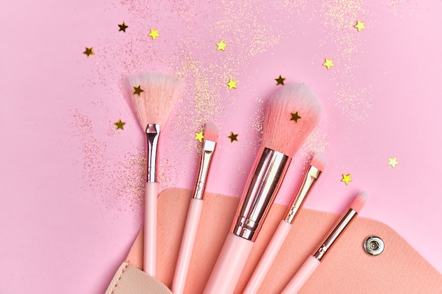 Makeup brushes in cosmetic bag and shiny sparkles on pink surface