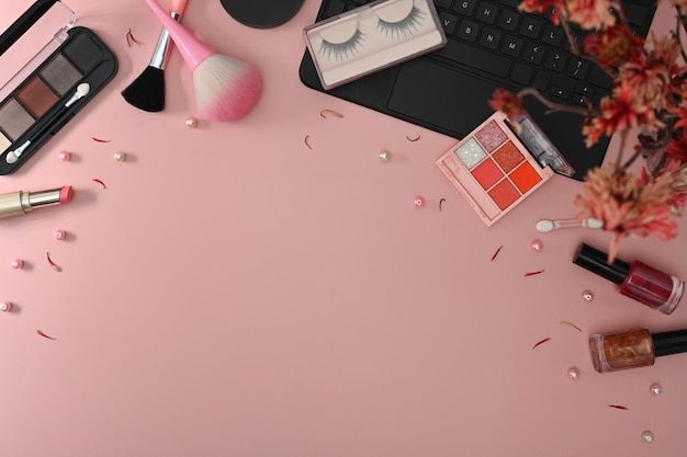 Makeup brushes cosmetics laptop and flowers on pink background Feminine workspace top view with copy space