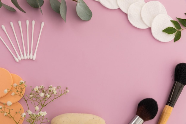 Photo makeup brushes, cotton buds, cotton pads and plants on pink background. beauty make up freshness copy space concept.