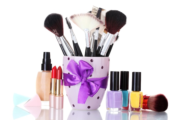 Makeup brushes in cup and cosmetics isolated on white