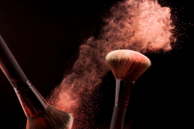 Makeup brushes in dust of red powder on dark background