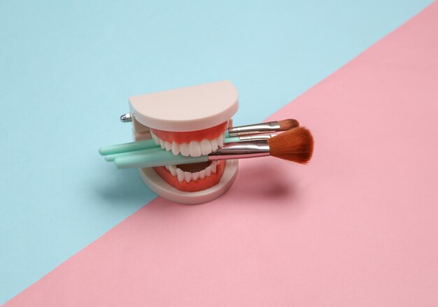 Photo makeup brushes in teeth of jaw model blue pink pastel background beauty minimal concept creative layout