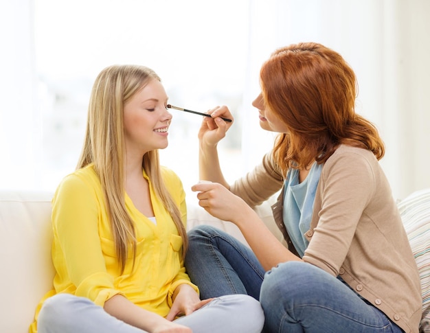 makeup, friendship and leisure concept - two smiling teenage girls applying make up at home