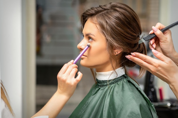 Processo di trucco e acconciatura. truccatore e parrucchiere che preparano giovane donna caucasica, lavorando in tandem.