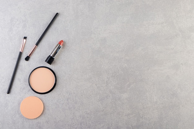 Makeup powder in black round plastic case with lipstick and brushes .