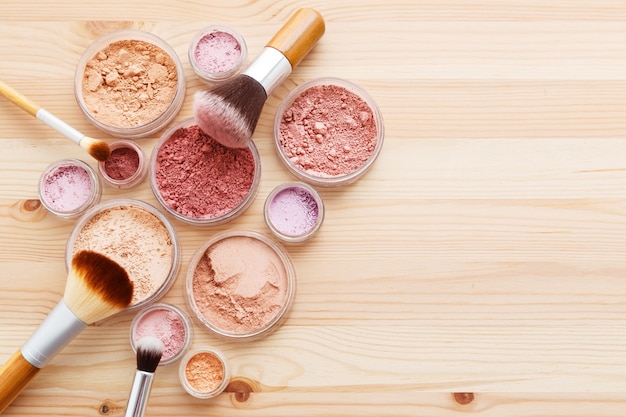 Makeup powder and brushes on wood background