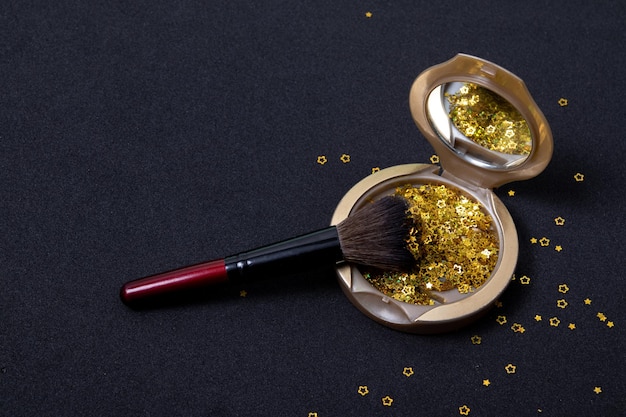 Makeup powder and cosmetic brush with golden stars on black background. Happy New Year greeting card