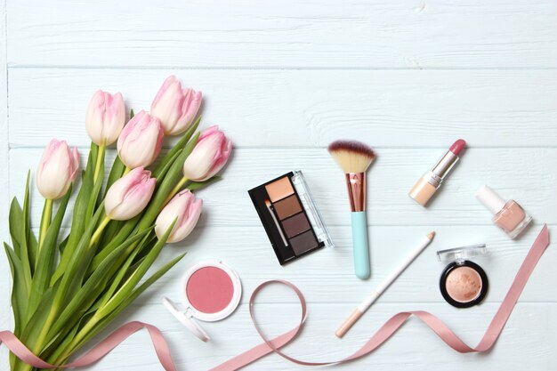 Makeup products and beautiful spring flowers on wooden background top view