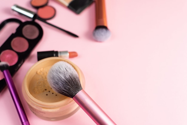 Makeup products and brushes on a pink background