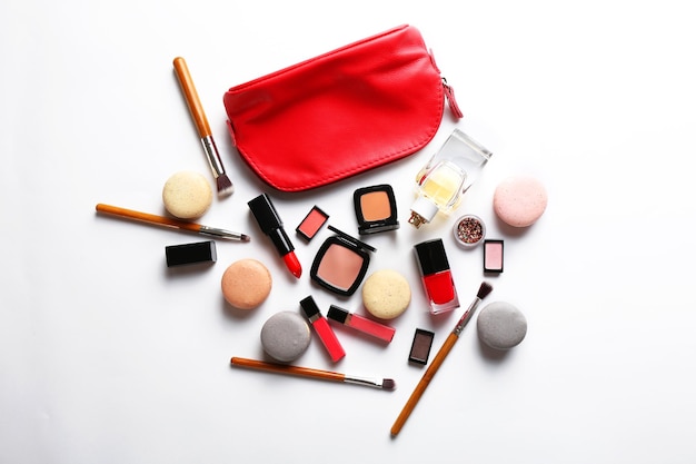 Makeup products with cosmetic bag and macaroons on light background