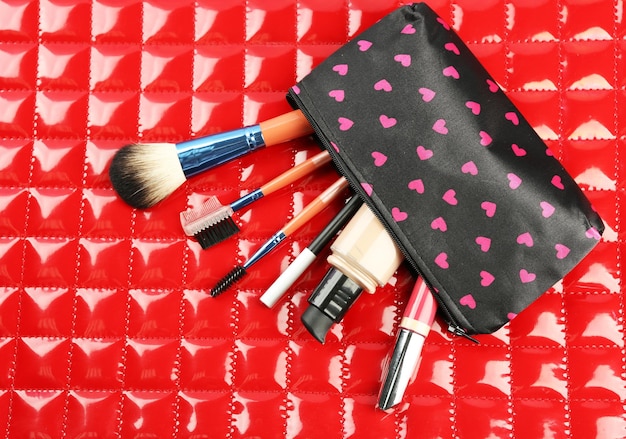 Makeup set with beautician brushes and cosmetics on red background