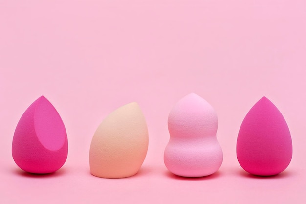 Makeup sponges of different colors and different shapes on a pink background