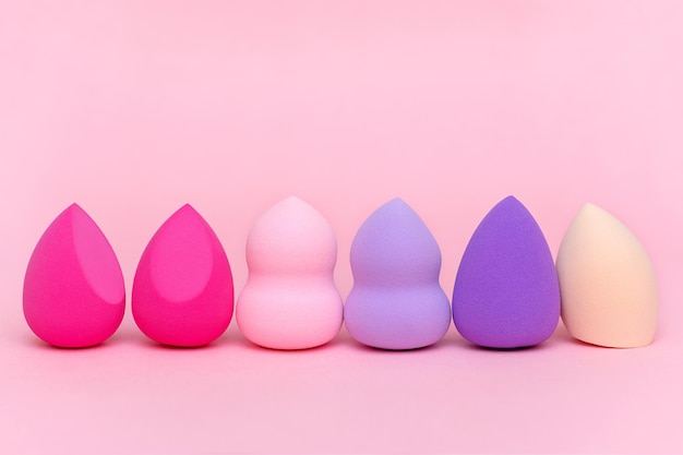 Makeup sponges of different shapes and colors on a pink background