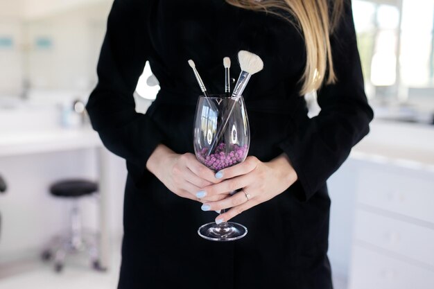 Photo makeup tools makeup concept the girl is holding a glass in which there are brushes brushes for the face