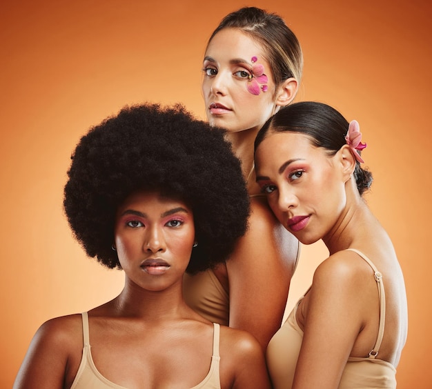 Makeup women and beauty diversity and flowers on orange studio background Models skincare and friends together with serious facial expression organic cosmetics or empowerment with floral orchids