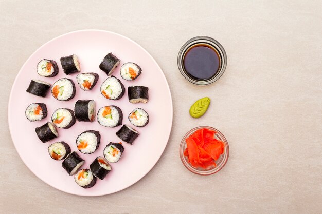 Maki rolletjes met gember, wasabi en sojasaus op een rosé bord