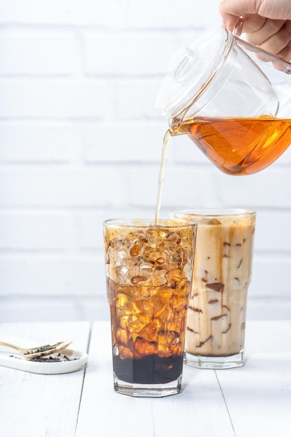 Making bubble tea pouring blend milk tea into brown sugar pattern drinking glass cup on white wooden table background close up copy space