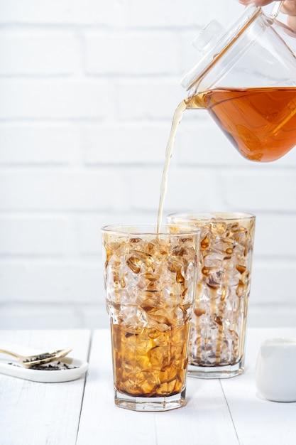 Photo making bubble tea, pouring blend milk tea into brown sugar pattern drinking glass cup on white wooden table background, close up, copy space