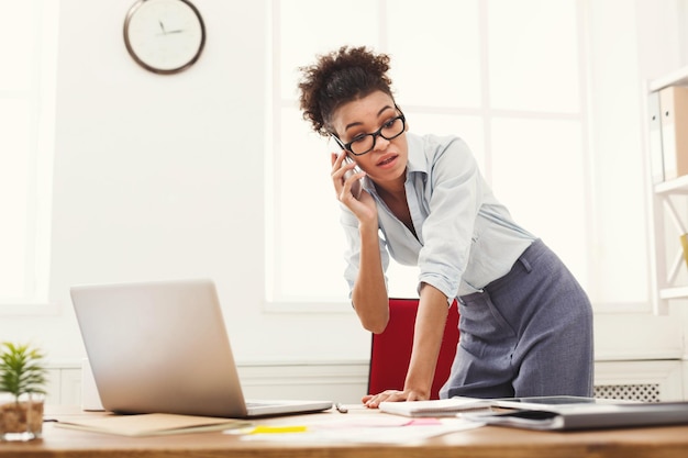 Making business call. Disappointed african-american ceo businesswoman talking on mobile in modern office, copy space.