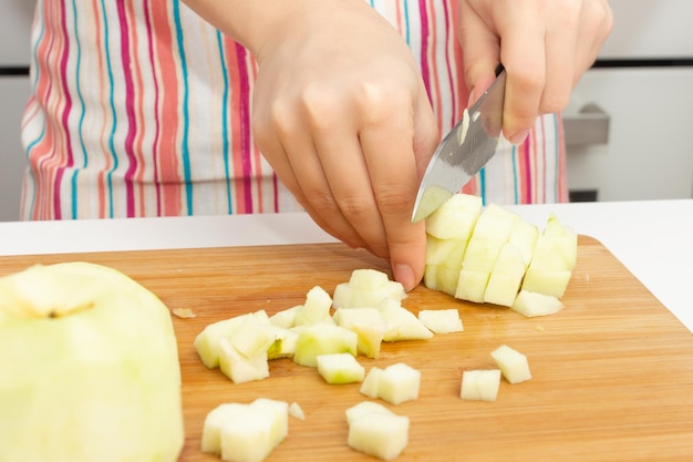 Making a cake. Girl cuts green apples with a knife in the kitchen