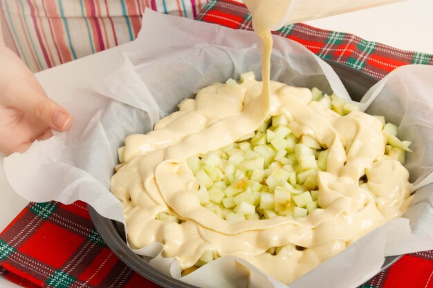 making a cake. girl pours green apples into cooked dough.