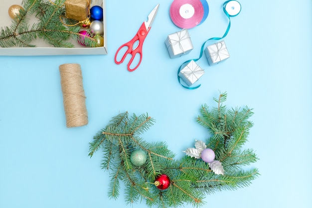 クリスマスリースを作る。トウヒの枝、装飾品、はさみ。青い背景。