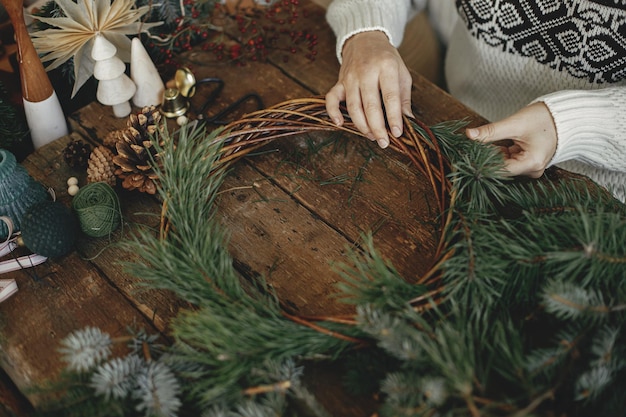 クリスマス リースを作る松の枝を保持し、素朴な背景にクリスマス リースを配置する女性