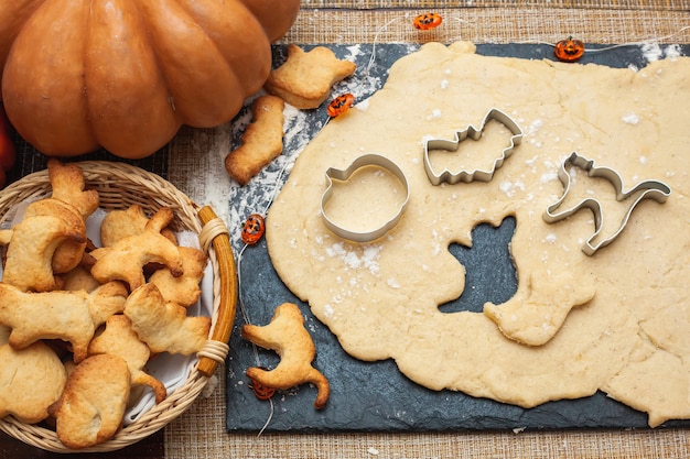 Making cookies for Halloween. Cut out cookies from dough in the form of pumpkin, cat, ghost and bat.