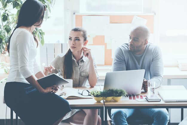 Making decisions together. Three young business people in smart casual wear discussing something while sitting at the office desk together