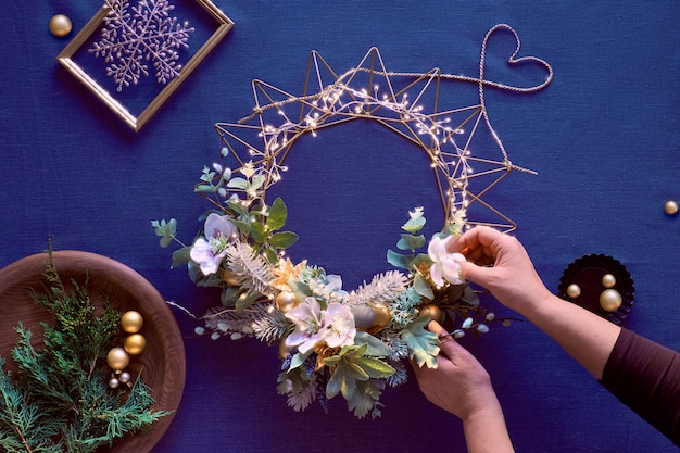 Making of decorative Christmas wreath on classic blue linen. Female hands make handmade wreath.