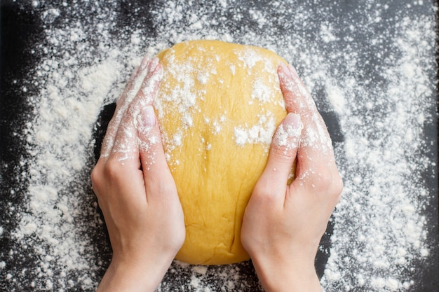 Making dough by female hands on black background