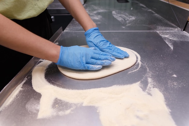 테이블 배경에 파란색 고무 장갑을 끼고 남성 손으로 반죽 만들기 피자 메이커는 피자 반죽을 준비합니다