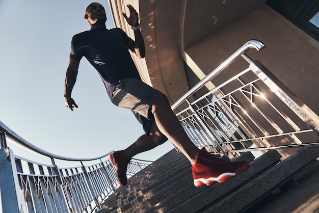 努力する。屋外で運動しながら階段を駆け下りるスポーツウェアの若いアフリカ人の全長