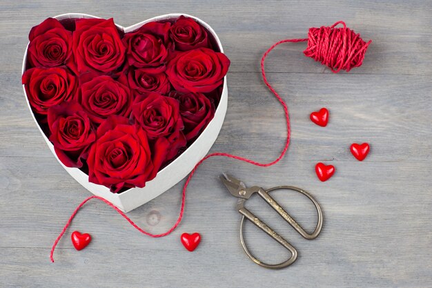 making a flower arrangement: scissors, ribbon, hearts, red roses, a heart-shaped box