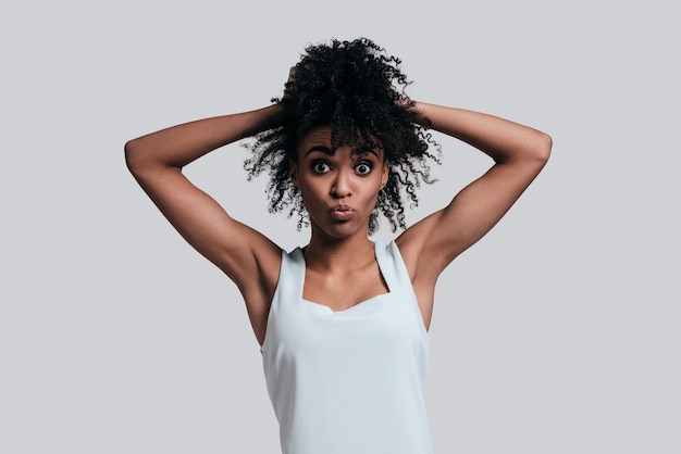 Making funny faces. Playful young African woman in casual wear keeping hands in hair 