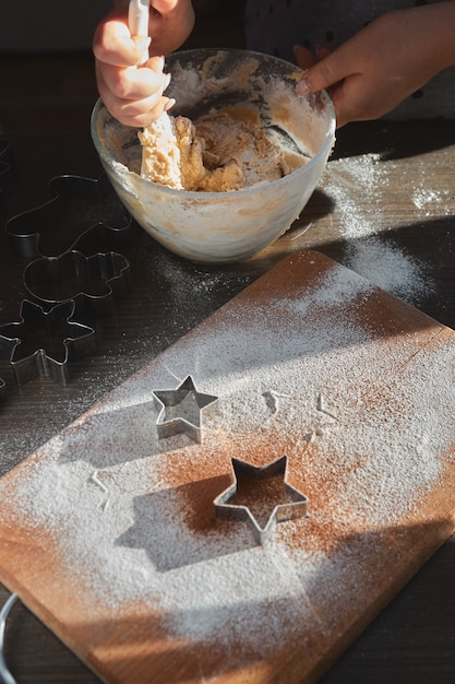 Foto preparare l'impasto per biscotti allo zenzero. le mani di una giovane donna si mescolano in una lastra di vetro per cuocere la pasta degli uomini di pan di zenzero. il concetto di una festa in casa, una cena in famiglia.