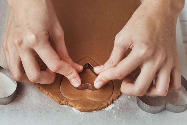 Making gingerbread cookies in shape of a heart for Valentines Day. Woman hand use cookie cutter. Holiday food concept