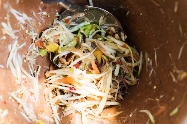 Realizzazione di insalata di papaya verde, som tam, cibo thai, ingredienti che si mescolano e martellano in un mortaio.