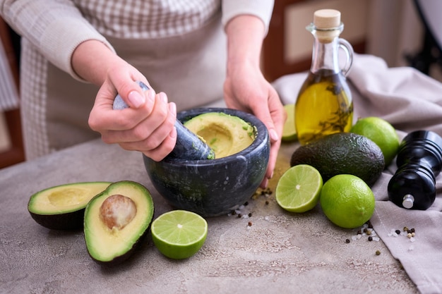 Making guacamole woman holding pestle to crush avocado in marble mortar on grey concrete table