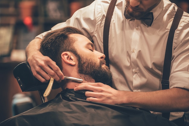 making hair look magical. close-up side view of young bearded man getting shaved 