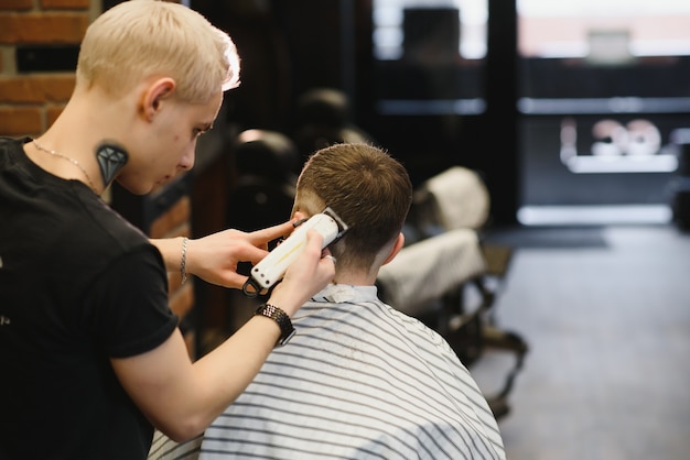 Making haircut look perfect. Young bearded man getting haircut by hairdresser while sitting in chair at barbershop