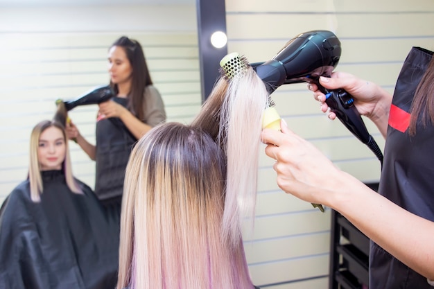 Making hairstyle using hair dryer. girl with blond long hair in a beauty salon. barbershop.