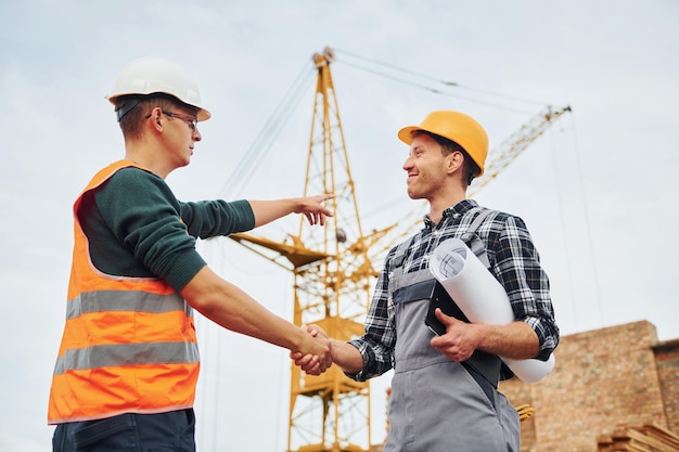 Making handshake Two construction workers in uniform and safety equipment have job on building together