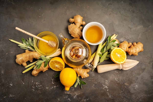 Preparare un tè antiossidante e antinfiammatorio sano con zenzero fresco, citronella, salvia, miele e limone su sfondo scuro con spazio di copia. vista dall'alto.